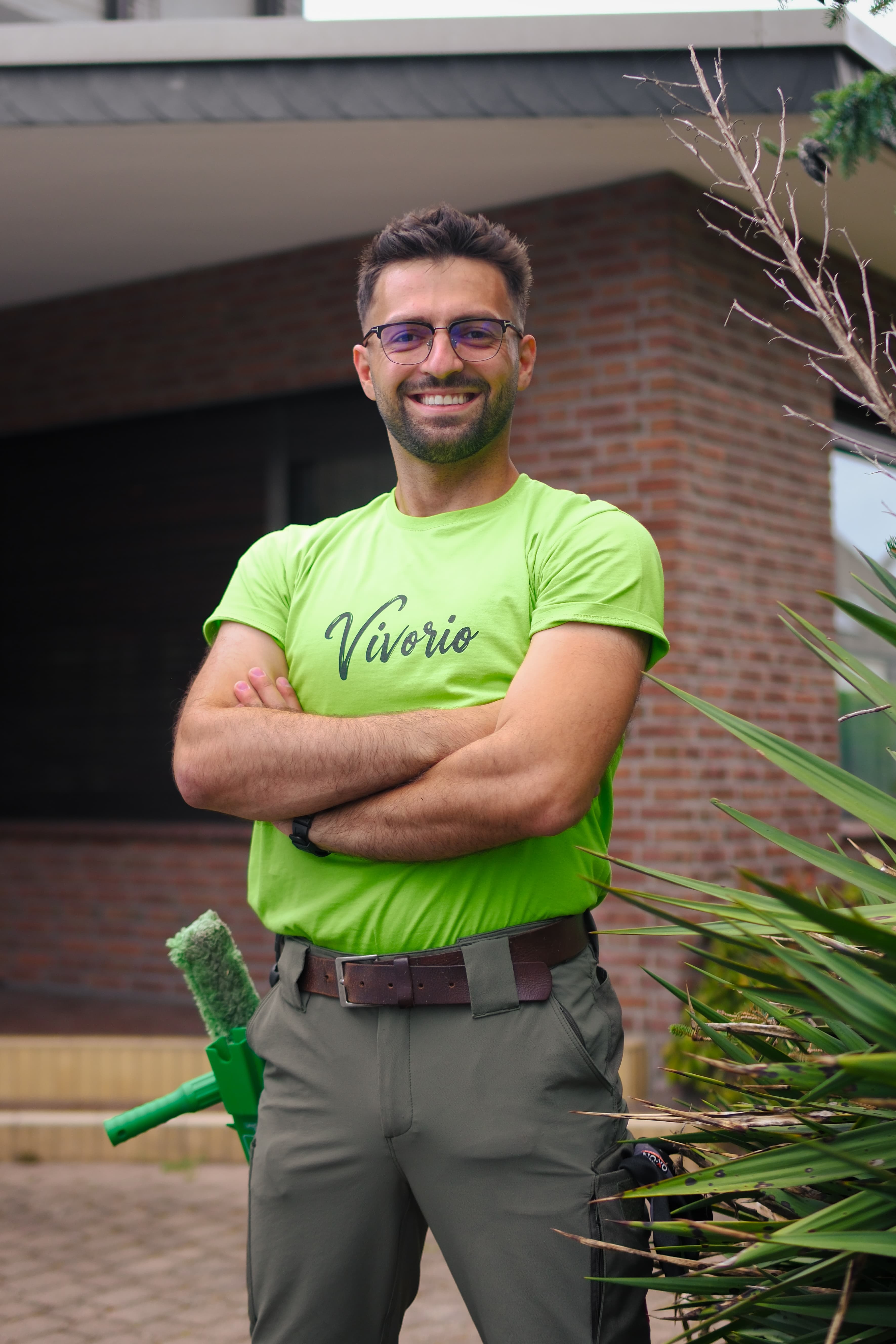 Mitarbeiter von Vivorio im hellgrünen Shirt vor einem Wohnhaus, mit Fensterwischer am Gürtel.